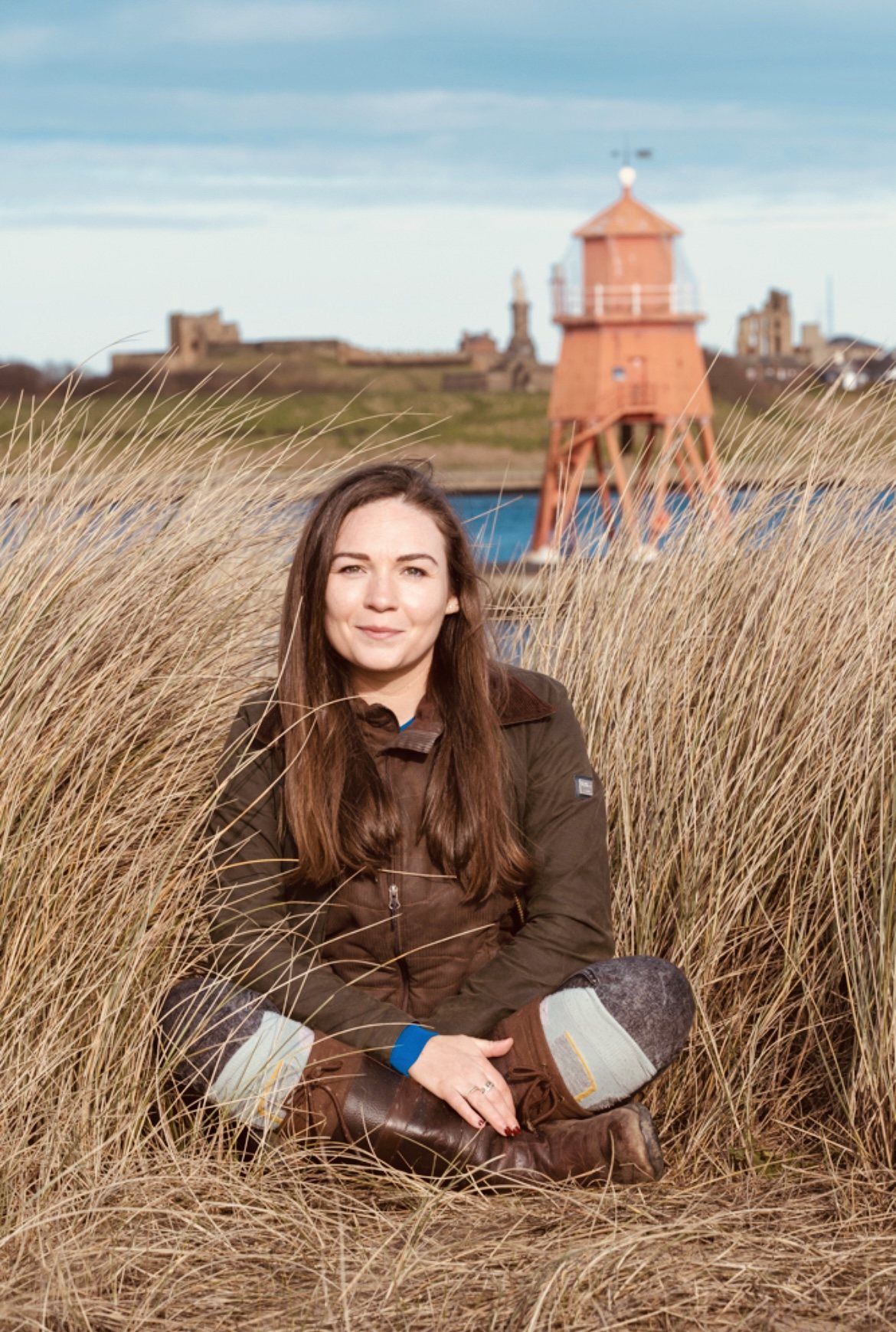 Georgie sitting cross-legged in the dune grass by the sea