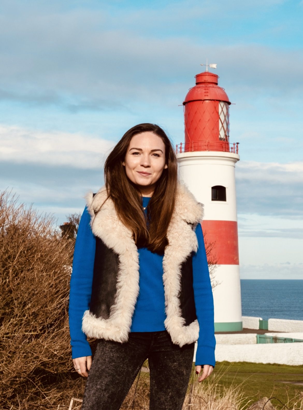 Georgie standing in front of a red and white lighthouse by the sea